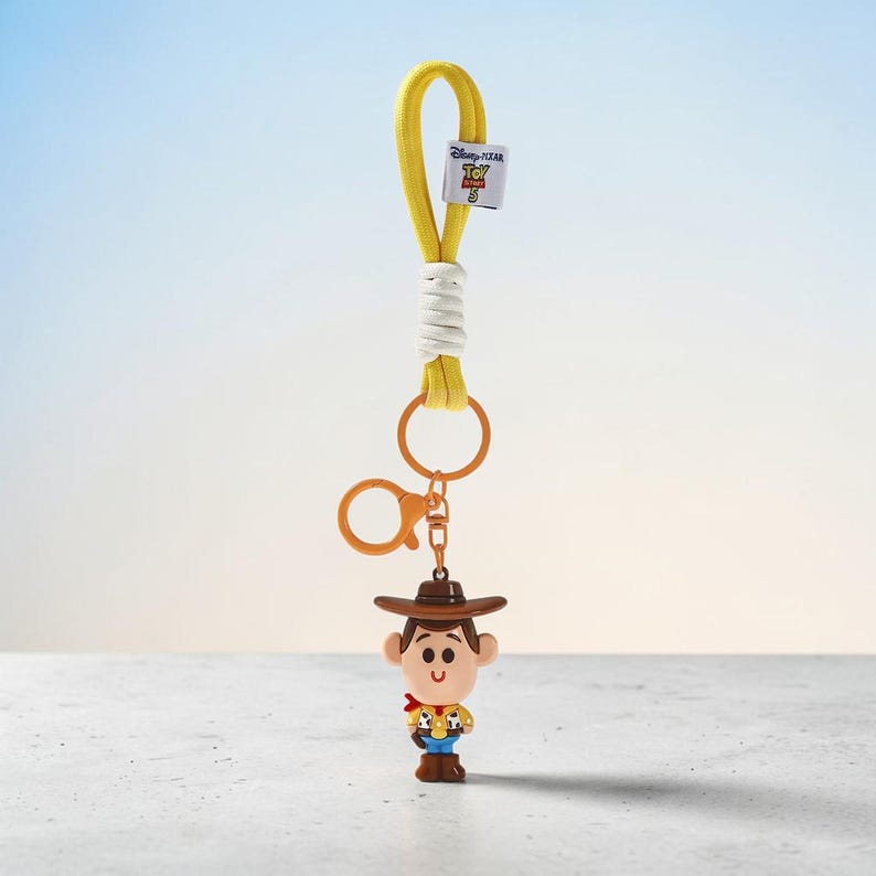 Puede incluir: Un llavero con una peque&ntilde;a figura de Woody de Toy Story 5, unido a una anilla de pl&aacute;stico naranja y un lazo de tela amarilla con un cord&oacute;n blanco. Incluye una peque&ntilde;a etiqueta blanca con el logotipo de Disney Pixar Toy Story 5.