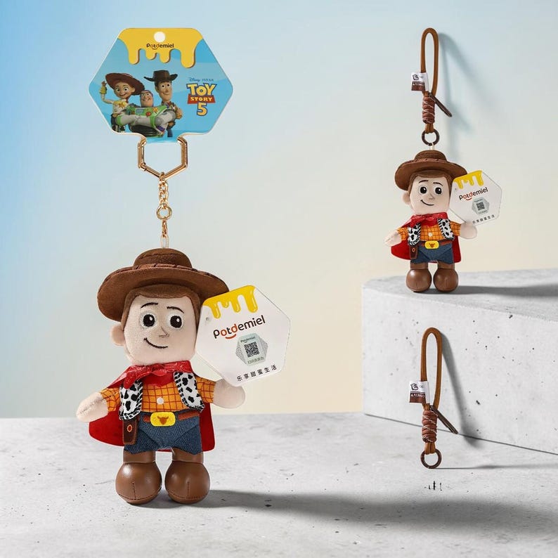 Puede incluir: Un llavero de peluche de Woody de Toy Story 5 con sombrero de vaquero marr&oacute;n, camisa de cuadros amarilla, chaleco con estampado de vaca, pantalones azules y capa roja. Incluye una cadena dorada, una etiqueta hexagonal Potdemiel y una tarjeta.