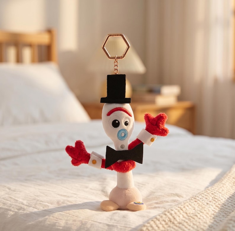 May include: A plush character keychain featuring a white spork-shaped body with a black top hat, a black bowtie, red pipe cleaner arms with three-fingered hands, and a gold-toned hexagonal ring attachment for securing to bags or keys.