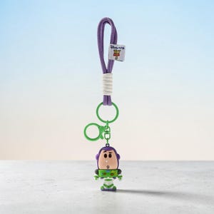 Puede incluir: Un llavero de cord&oacute;n morado con un peque&ntilde;o dije del personaje Buzz Lightyear. El cord&oacute;n tiene un detalle envuelto en blanco y una peque&ntilde;a etiqueta blanca con el logotipo de Disney Pixar Toy Story 5. Incluye una argolla y un mosquet&oacute;n verdes.