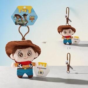Puede incluir: Un llavero de peluche de Woody de Toy Story 5 con sombrero de vaquero marr&oacute;n, pa&ntilde;uelo rojo, camisa amarilla con estampado de vaca negro y pantalones azules. El personaje tiene grandes ojos marrones y una correa marr&oacute;n con una etiqueta hexagonal.