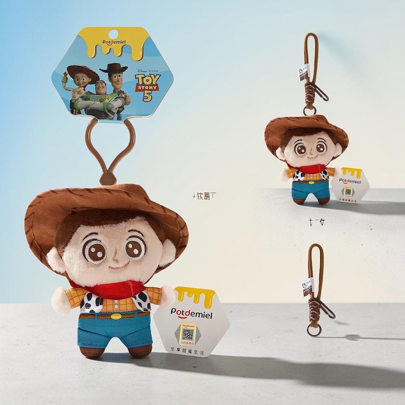 Puede incluir: Un llavero de peluche de Woody de Toy Story 5 con sombrero de vaquero marr&oacute;n, pa&ntilde;uelo rojo, camisa amarilla con estampado de vaca negro y pantalones azules. El personaje tiene grandes ojos marrones y una correa marr&oacute;n con una etiqueta hexagonal.