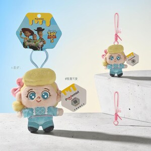 Puede incluir: Un llavero de peluche con un personaje de cabello rubio, un lazo rosa y un traje azul claro. El producto incluye una etiqueta hexagonal con el logo de Potdemiel y un c&oacute;digo QR, adem&aacute;s de una correa rosa y una tarjeta de Toy Story 5.