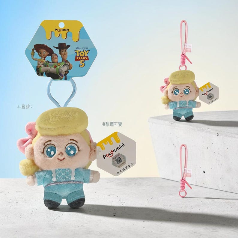 Puede incluir: Un llavero de peluche con un personaje de cabello rubio, un lazo rosa y un traje azul claro. El producto incluye una etiqueta hexagonal con el logo de Potdemiel y un c&oacute;digo QR, adem&aacute;s de una correa rosa y una tarjeta de Toy Story 5.