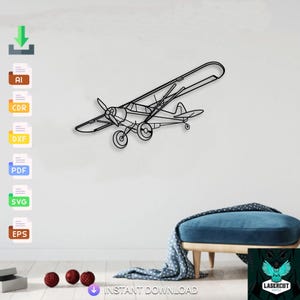 Puede incluir: Una pieza de arte mural de avión de metal negro. El diseño del biplano presenta una hélice, alas y cola, montada en una pared blanca. Las palabras "DESCARGA INSTANTÁNEA" son visibles en la parte inferior de la imagen.