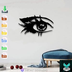 May include: Black, laser-cut eye wall art. The eye features detailed eyelashes and iris, creating a striking decorative piece. The design is mounted on a white wall, with a blue ottoman and decorative items in the foreground.