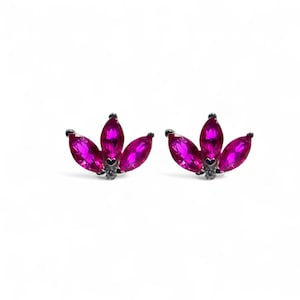 Op de afbeelding: Een paar oorstekers met een bloemmotief. Elke oorbel heeft drie marquise-geslepen, levendige fuchsia-kleurige edelstenen, gezet in een zilverkleurig metaal. De oorbellen worden gepresenteerd tegen een witte achtergrond.