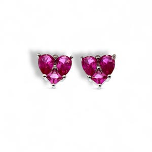 May include: A pair of silver stud earrings. Each earring has three magenta gemstones: two pear-shaped and one square-cut. The earrings are set on a white background. The gemstones are a vibrant shade of pink.