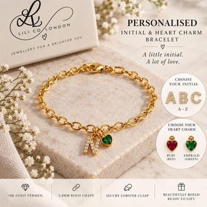 May include: A gold-toned rolo chain bracelet featuring a dangling letter N charm encrusted with small clear stones and a small green heart-shaped charm. The bracelet includes a secure lobster clasp and is presented with options for custom initials.