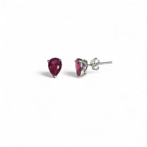 May include: A pair of silver stud earrings, each with a pear-shaped, deep red gemstone. The earrings are set in a simple design, highlighting the vibrant colour of the stones. The studs are displayed against a white background.