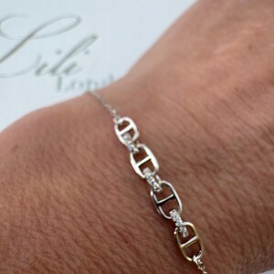 May include: A silver bracelet with a chain link design featuring small clear stones. The bracelet is on a person's wrist.