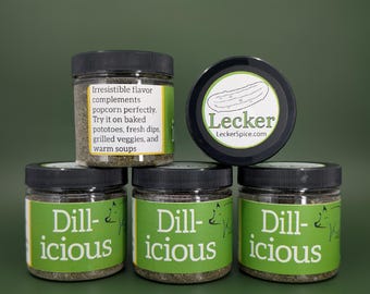 Peut inclure: Trois bocaux en verre d'assaisonnement au dill, étiquetés "Dill-icious", sur un fond vert. Le bocal du haut a un couvercle noir avec une étiquette blanche qui dit "Lecker" et "LeckerSpice.com". L'étiquette contient également un dessin de cornichon.