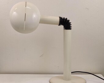 May include: White table lamp with a round, white shade and a flexible, black and white arm. The lamp has a white base with a round, white platform.