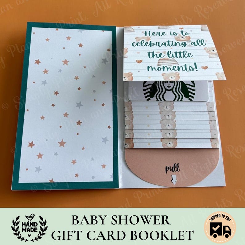 May include: A paper gift card booklet featuring a left panel with a white background and scattered brown and gray stars. The right panel displays a pull-tab mechanism with a bear pattern, the text "Here is to celebrating all the little moments!", and a Starbucks gift card.