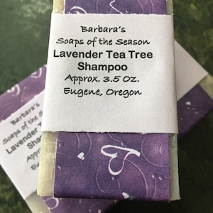 May include: A bar of lavender tea tree shampoo wrapped in purple paper with white text that reads "Barbara's Soaps of the Season Lavender Tea Tree Shampoo Approx. 3.5 oz. Eugene, Oregon"