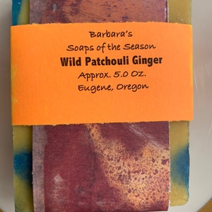 May include: A bar of soap with an orange label that reads "Barbara's Soaps of the Season Wild Patchouli Ginger Approx. 5.0 OZ. Eugene, Oregon." The soap has a colorful design with blue, yellow, and brown tones.