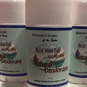 May include: A white deodorant stick with a blue label that says "Blue Man Bay Plus Bay Rum Natural Deodorant" and "Barbara's Soaps of the Season". The label also includes a small sailboat graphic and the website address "www.barbarasoaps.com".