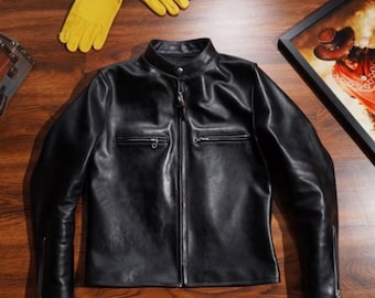 May include: Black leather jacket with a stand-up collar, zipper closure, and two front pockets. The jacket has a classic design and is displayed with yellow leather gloves and a framed picture.