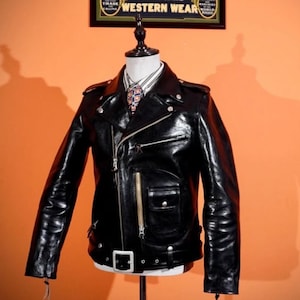 Op de afbeelding: Zwarte leren motorjas met een glanzende afwerking. De jas heeft een asymmetrische ritssluiting, meerdere zakken en een ceintuur. De jas wordt gepresenteerd op een paspop met een stropdas met patroon en een wit overhemd.