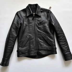 May include: A black leather jacket featuring a pointed collar, a full-length front zipper, and long sleeves with cuffs. The jacket includes a single zippered chest pocket on the left side and two slanted zippered pockets at the waist area.