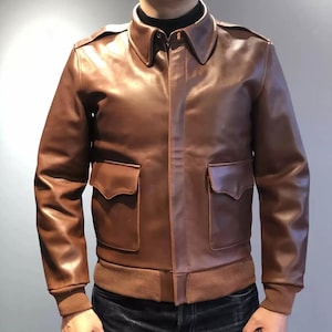 Könnte beinhalten: Braune Lederjacke mit klassischem Design. Die Jacke hat einen Kragen, zwei Vordertaschen sowie einen gerippten Saum und Bündchen. Die Jacke ist aus geschmeidigem Leder gefertigt.