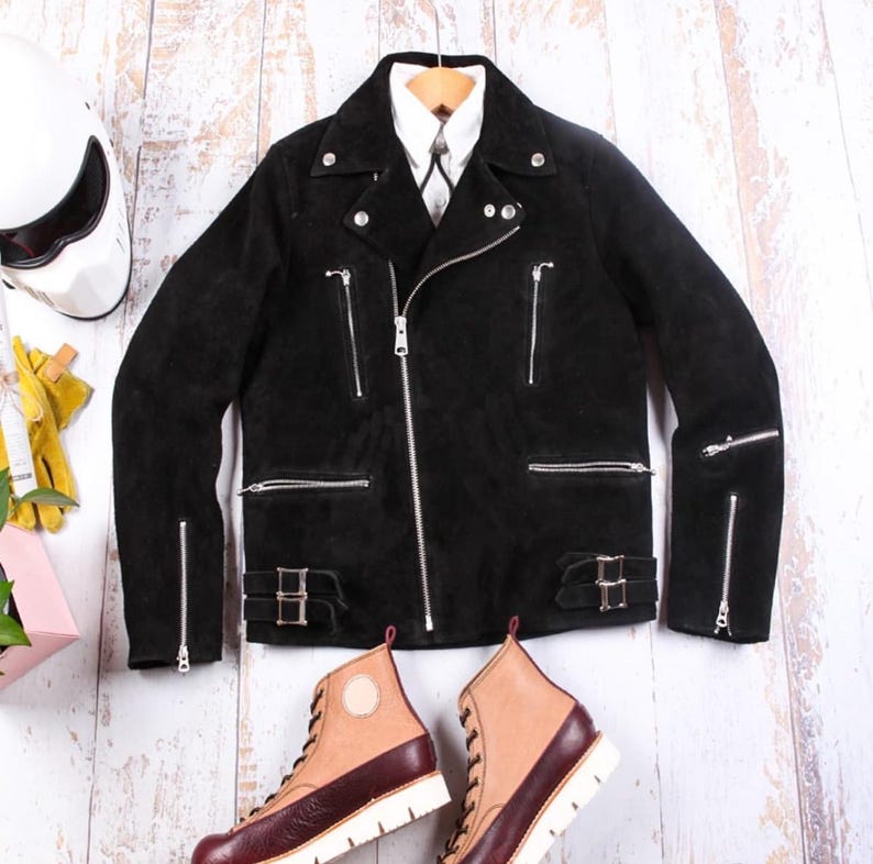 May include: A black suede motorcycle jacket with silver zippers and buckles, paired with brown and burgundy leather boots. A white helmet and yellow gloves are visible, suggesting a biker theme.
