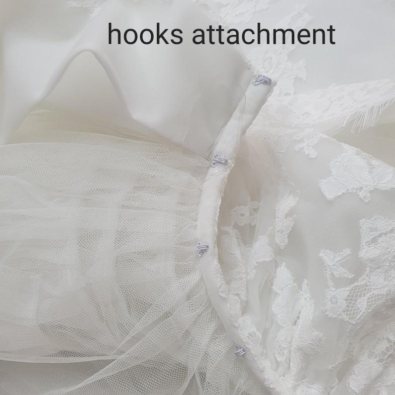 May include: Close-up of a white bridal gown detail. The image shows the hooks attachment of the dress, with delicate lace and tulle. The text "hooks attachment" is visible.