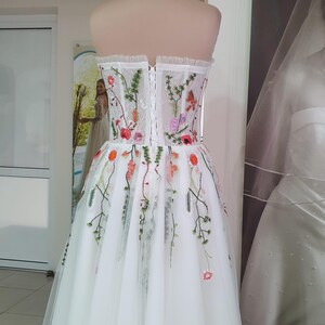 May include: A white strapless wedding dress with a tulle skirt and floral embroidery. The dress has a fitted bodice with a lace-up back.