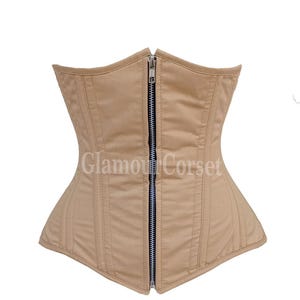 Może przedstawiać: Beżowy gorset z zapięciem na zamek z przodu i pionowymi przeszyciami. Gorset zawiera napis "Glamour Corset" i jest przeznaczony do modelowania talii. Odzież wykonana jest z gładkiej tkaniny.