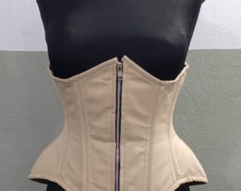 Op de afbeelding: Een beige corset met een ritssluiting aan de voorkant, weergegeven op een zwarte mannequin. Het corset heeft een gestructureerd ontwerp met verticale naden en een licht puntige onderrand. De mannequin staat op een metalen standaard.