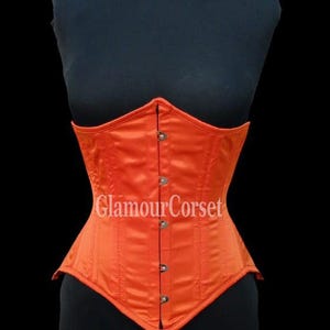 May include: An orange satin corset with vertical stitching and a row of buttons down the front. The corset is displayed on a black mannequin. The text "GlamourCorset" is printed on the front.