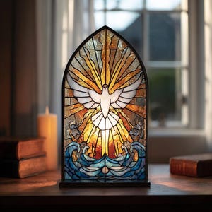 Può includere: Un pannello in vetro colorato raffigurante una colomba bianca con ali spiegate, irradiante luce dorata. Sotto, onde blu. Il pannello, incorniciato in nero, è posto su una superficie di legno, evocando spiritualità e pace.