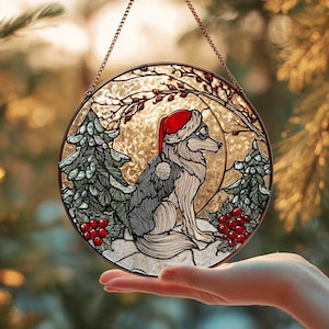 Pode incluir: Uma janela redonda de vitral com um lobo usando um gorro de Papai Noel, cercado por folhagens e bagas de inverno. A obra de arte é em tons de cinza, vermelho e verde, com um fundo dourado e uma corrente de cobre para pendurar.