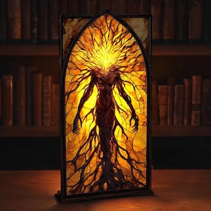 May include: A stained glass panel depicting a humanoid figure with a tree-like form. The figure is brown with yellow and orange highlights, and the panel is framed in dark wood. The artwork is illuminated from behind, creating a warm, glowing effect. The panel is standing on a wooden surface.