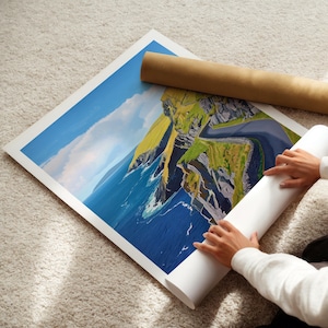 A person's hands are holding a roll of paper, which appears to be a painting of a coastal landscape with cliffs and the ocean.