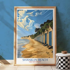 May include: A framed print featuring Shanklin Beach, Isle of Wight. The artwork shows a sunny beach with golden sand, rows of blue beach huts, and a sky filled with clouds. The text "SHANKLIN BEACH" and "ISLE OF WIGHT" are displayed at the bottom.