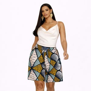 Könnte beinhalten: Eine Frau trägt ein weißes Oberteil mit Wasserfallausschnitt und gemusterte Shorts. Die Shorts haben ein geometrisches Design in Gelb, Blau und Weiß. Das Outfit ist ein stilvolles Ensemble.