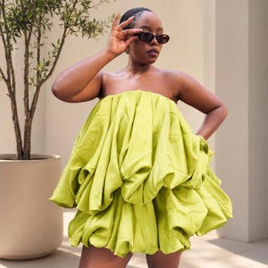 May include: A strapless lime green mini dress featuring a voluminous, gathered bubble silhouette with multiple layers of fabric. The garment has a smooth, satin-like texture and a short hemline that sits above the knees, creating a full, rounded shape.