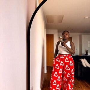 Puede incluir: Pantalones rojos de pernera ancha con un estampado de triángulos blancos. Los pantalones se combinan con una camiseta sin mangas blanca. La imagen está tomada frente a un espejo.