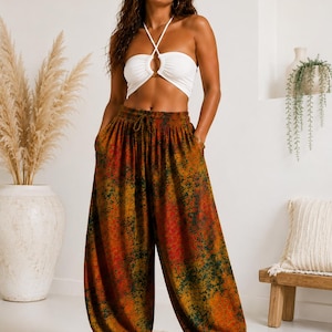 Puede incluir: Una mujer con un top halter blanco y pantalones harén estampados. Los pantalones presentan una vibrante mezcla de tonos naranja, rojo y verde. El top tiene un detalle circular en el centro. Los pantalones tienen cintura con cordón y tobillos fruncidos.