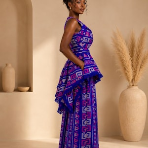 May include: A sleeveless floor-length dress in vibrant royal blue, featuring a repeating geometric pattern in shades of magenta, white, and light blue. The garment includes a structured peplum waist detail with a fringed hem and a straight skirt.