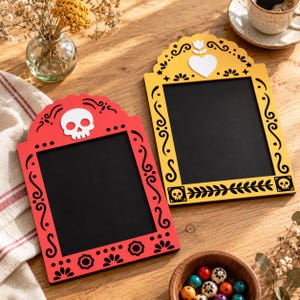 May include: Two rectangular chalkboard signs with arched tops. One frame is red with a white skull cutout at the top, and the other is yellow with a white heart and flower cutout. Both feature black scrollwork patterns and black chalkboard surfaces.