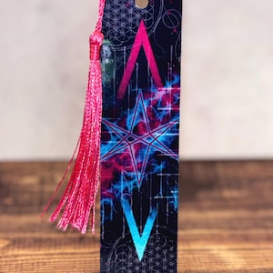 May include: A rectangular bookmark with a dark blue background featuring a pink and blue star design. The bookmark has a pink tassel attached to the top. The design includes geometric shapes and a celestial theme.