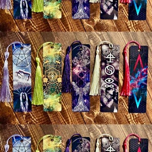 May include: A collection of decorative bookmarks with colorful designs and tassels. Each bookmark features unique artwork, including celestial symbols, angel figures, and abstract patterns. Tassels are in various colors, such as purple, green, and red.