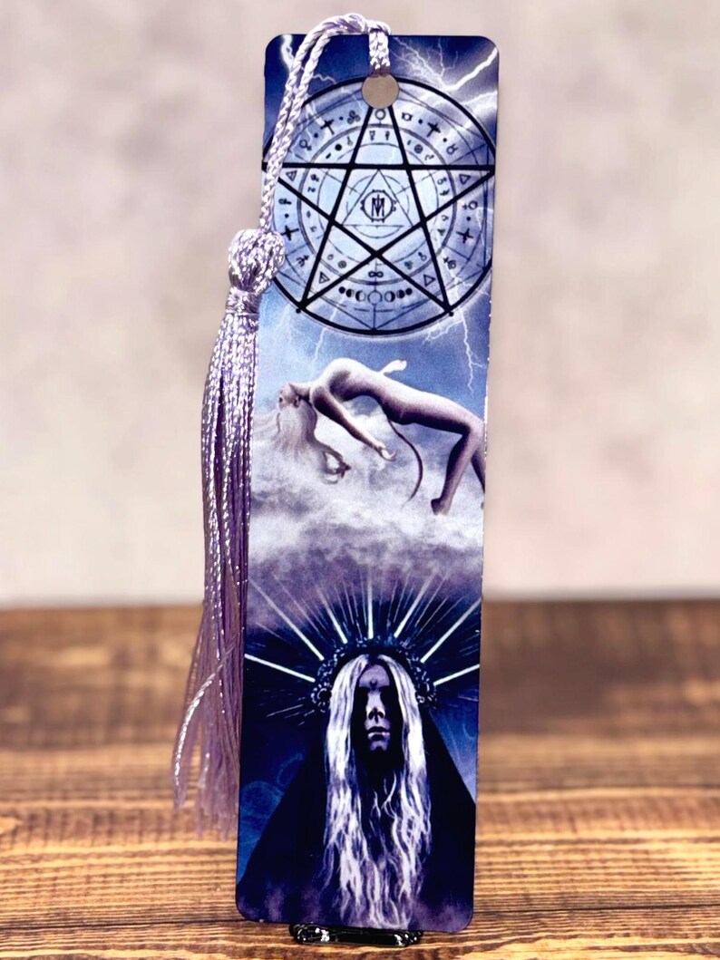 May include: A rectangular bookmark with a purple tassel and cord. The bookmark features a celestial design with a pentagram, a figure floating in clouds, and a portrait of a person with a crown. The background is blue with lightning.