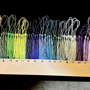 May include: A collection of 30 colorful tassels arranged in a rainbow spectrum, each with a looped string for hanging. The tassels range in color from red to black, with a white numbered guide below each tassel.