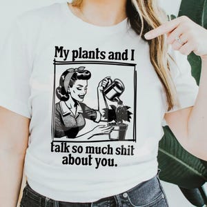 May include: White t-shirt with a black and white graphic of a woman watering a plant, with the text "My plants and I talk so much shit about you." The graphic is in a retro style.