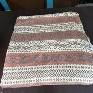 May include: Folded fabric with a geometric pattern in shades of brown, white, and gray. The design features repeating diamond and zigzag motifs, creating a textured appearance. The fabric appears to be a knit or woven material.