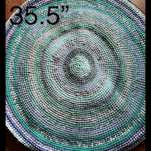 May include: A round, crocheted rug with a multi-colored design in shades of blue, green, and white. The rug has a diameter of 35.5 inches.