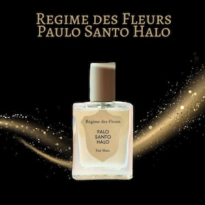 May include: A clear glass perfume bottle with a beige cap and a shield-shaped label. The label features the text Regime des Fleurs, PALO SANTO HALO, and Fait Main. The bottle is centered against a black background with a golden light effect.